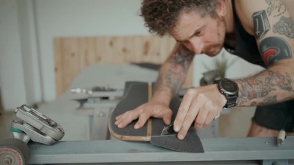 Soft focus beautiful cinematic shot of urban skateboarder or millennial hipster in designer loft studio or wokshop, work on regripping old skateboard and attaching new tape. Concept diy