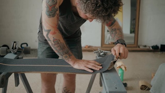 Soft focus beautiful cinematic shot of urban skateboarder or millennial hipster in designer loft studio or wokshop, work on regripping old skateboard and attaching new tape. Concept diy