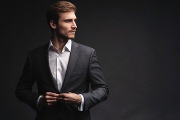 Portrait of serious handsome man in gray suit buttoning jacket