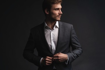 Portrait of serious handsome man in gray suit buttoning jacket