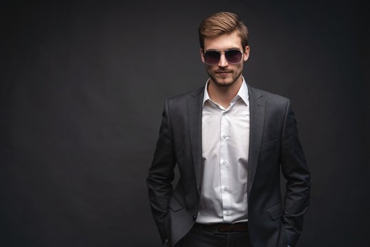 Stylish young man in suit and sunglasses. Business style. Office worker. Sexy man standing isolated over gray background