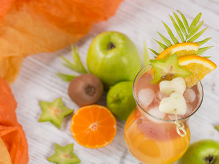 Summer cocktail with various tropical fruits around. Apple, kiwi, tangerine, orange, mango, carambola.
