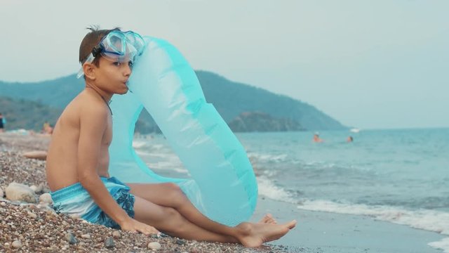 Young boy sitting on sea beach. Little boy preparing inflatable circle for swim