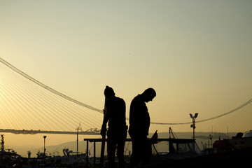 Fototapeta na wymiar Fishermen make repair under the bosphorus bridge at sunset 