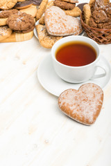 romantic tea party on Valentines day. sweet heart shaped cookies and cup of tea on white wooden table. vertical view, copy space