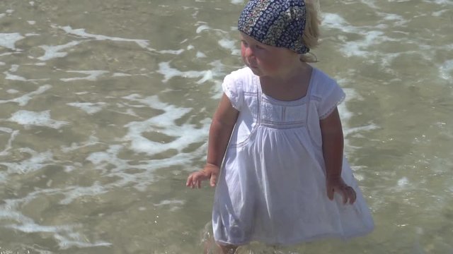 A child is standing in the sea water. Little girl in a white dress walks in the sea water.