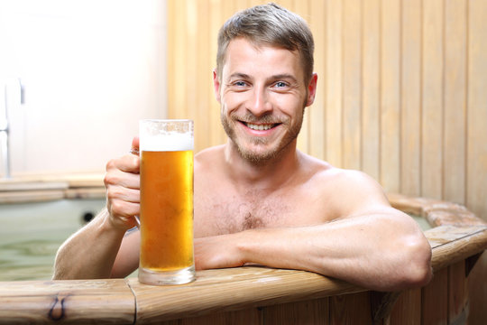 Męskie spa. Przystojny mężczyzna zażywa kąpieli w bali z woda termalną pijąc piwo kuflowe.