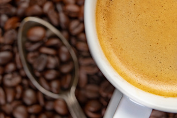 Grains of coffee and white cup of brewed coffee. Tasty foam on the surface of a delicious drink.