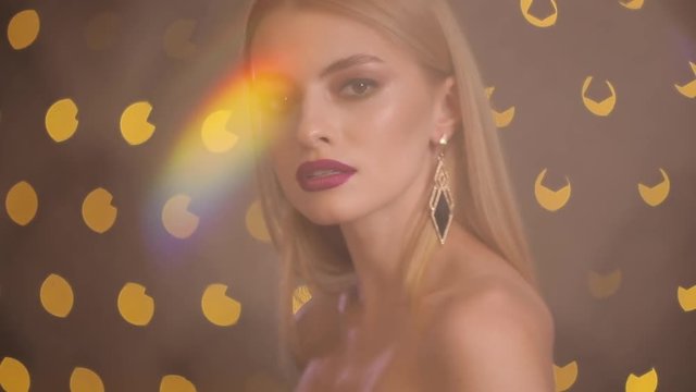 Pretty attractive fashion model with beautiful blonde hair and nice face posing in yellow lights bokeh, studio shot, slow motion