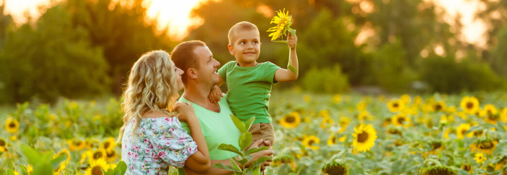 Happy family having fun in the field of sunflowers. Father hugs his son. Mother holding sunflower. outdoor shot