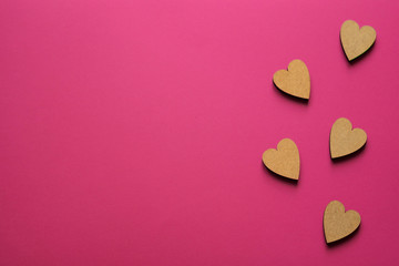 Little wooden hearts on pink background. Romantic composition with copy space for greeting.