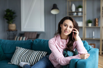 Smiling woman sitting on sofa in the living room having a phone call.
