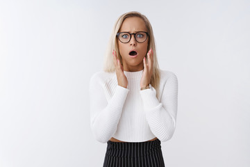 Blond woman in shock standing in stupor speechless from devestation being witness of terrible accident raising hands in fright and worry open mouth and frowning shook over white background