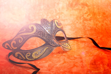 Mardi Gras mask on a bright, colorful orange background, closeup with lens flare.