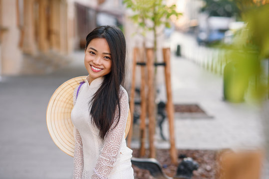 Close up portrait of pretty asian girl dressed in Ao Dai dress with vietnamese conical hat against arches background.