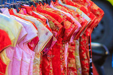 Beautiful Qipao (cheongsam dress or Chinese dress) for women hanging on a clothes line in night market for sale to customers during the festival is Chinese New Year at Bangkok, Thailand.
