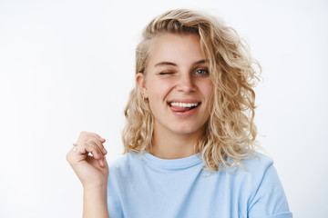Obraz premium Girl in flirty and happy mood winking and sticking out tongue playfully at camera as posing over white background, smiling having fun and enjoying life, leading carefree lifestyle over white wall