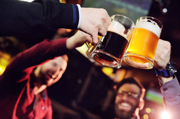 Happy male friends clinking with beer mugs in pub