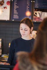 Attractive girl waiter, serves customers behind the counter. cake and people in cafe concept.