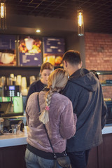 a loving couple, a man and a woman stand in front of the counter in the cafe and choose to order. cake and people in cafe concept.