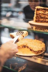 woman choosing sweet cakes at cafe and waiter picks up a piece of cake from the confectionery shop window. cake and people in cafe concept.