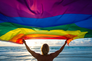 Colorful silhouette of a man with blond hair holding a gay pride rainbow flag blowing in the wind...