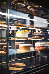 Showcase with sweets chocolate milk Strawberry fruit cakes for sale in cake shop. Different types Cake tray in showcase. Glass display at store bakery pastry shop.