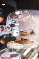Female waiter holds cookie in the metal pinch which is taken from the confectionery shop for the ordering of the client. Ideal background for advertising a coffee shop, a cafe, a restaurant