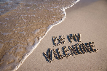 Fototapeta premium Be my Valentine message handwritten on a smooth sand beach with an oncoming wave
