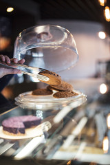 Female waiter holds cookie in the metal pinch which is taken from the confectionery shop for the ordering of the client. Ideal background for advertising a coffee shop, a cafe, a restaurant