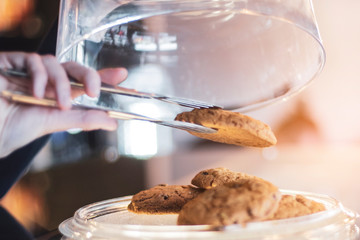 male hand open the glassware lid of the plate on which the delicious oatmeal cookies, in order for the buyer to choose a cake. The background for advertising a coffee shop, a cafe, a restaurant