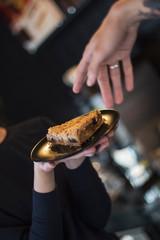 hand with fingers stretching to a plate with a dessert in another hand. Concept in the style of the...