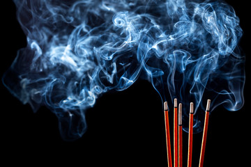 Closeup of calmly burning incense sticks with blue fume on black background - 248757599