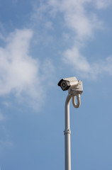 A cantilevered modern white security CCTV camera, pointing and checking to all coming visitors in a modern house&rsquo;s front gate during the day.