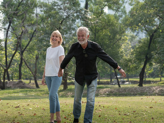 Happy senior man and woman couple walking and holding hands in a park on a sunny day. relax in the forest spring summer time. free time, lifestyle retirement grandparents concept.