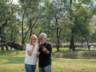 Obraz premium Happy senior man and woman couple in a park on a sunny day. relax in the forest spring summer time. free time, lifestyle retirement grandparents concept.