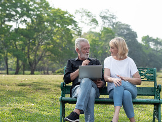 Senior man and woman couple connected on laptop computer in a park on a sunny day. relax in the forest spring summer time. free time, lifestyle retirement grandparents concept.