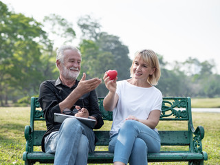 Senior man and woman couple give a heart in a park on a sunny day. Valentine's Day, Health, lifestyle, care, retirement grandparents concept.