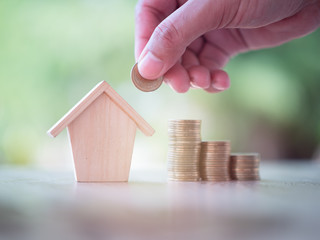 Hand putting money coins with home model on nature green background. Finance and house loan,...