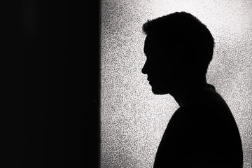 Silhouette of young thoughtful man stangin in a dark room. People emotions.