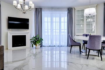 Minimalistic interior of living room in light tone with marble flooring, large windows and a table...