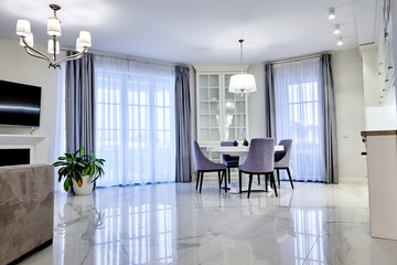 Minimalistic interior of living room in light tone with marble flooring, large windows and a table...