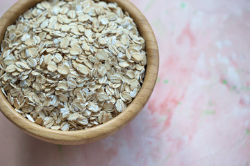 Uncooked oatmeal or oat flakes in a wooden bowl on a pink background