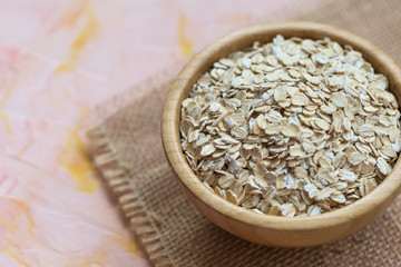 Uncooked oatmeal or oat flakes in a wooden bowl on a pink background