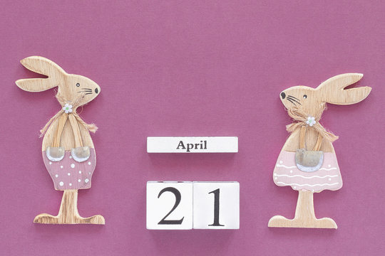 Wooden cubes calendar April 21 and pair of wooden easter bunnies on purple paper background. Concept Catholic Easter Copy space Template for lettering, text or your design Creative Top View.