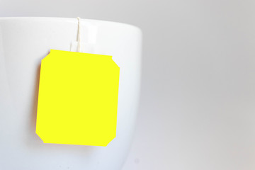 Close up of yellow label tea bag on the edge of the cup on grey background shot in studio.