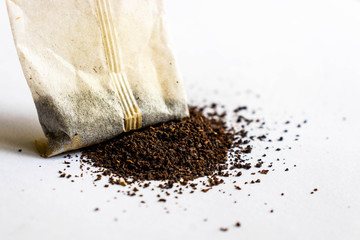 Macro close up of tea bag with dried tea leaves placed on grey background.