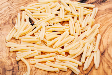 Uncooked Italian Casarecce pasta made from organic durum wheat semolina on natural olive wood cutting board. Macaroni product.