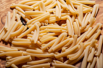 Uncooked Italian Casarecce pasta made from organic durum wheat semolina on natural olive wood cutting board. Macaroni product.