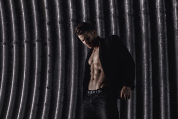 Fototapeta na wymiar Muscular young man with beard on dark tunnel urban background. Fashion portrait of brutal strong muscle guy with modern trendy hairstyle. Model, fashion concept. Sexy naked torso, six pack abs.